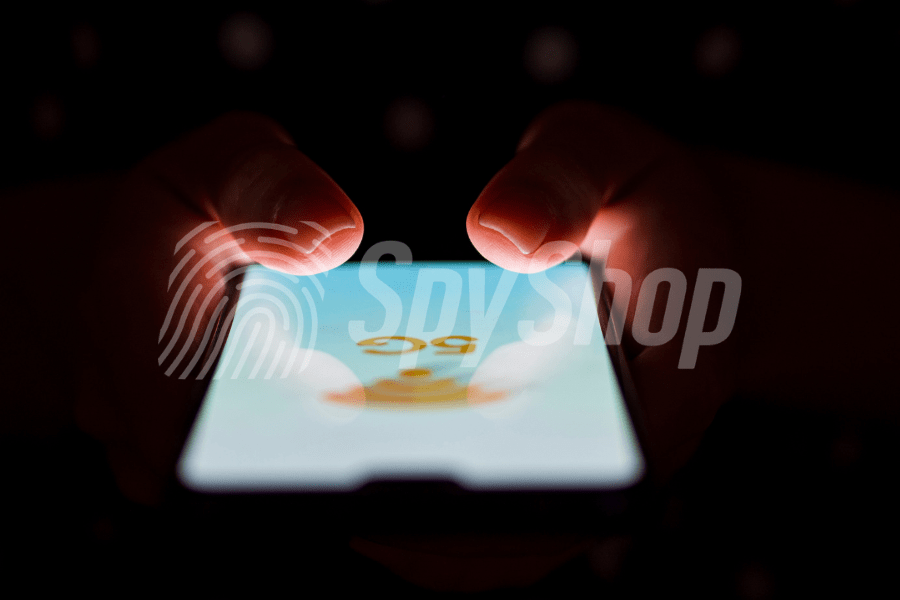 Close-up of the phone screen with 5G network signage. Hands visible above it, the background is dark.