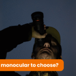 A man wearing a cap is holding a monocular and looking through it into the darkness. It is the middle of the night.